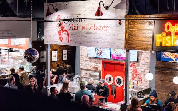 A group of people standing outside of the Cousins Maine Lobster restaurant location in the Morgan Street Food Hall in Raleigh, North Carolina.